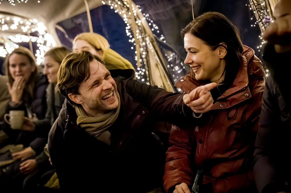 Lachend gezelschap met warme dranken op een overdekte boot tijdens een winteravond in Amsterdam