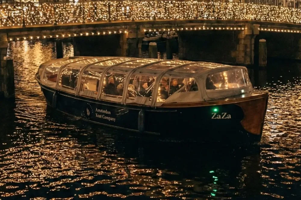 De Zaza met gesloten kap vaart 's avonds onder een brug door tijdens het Amsterdam Light Festival